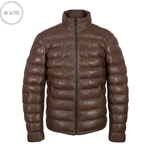 Puede incluir: Chaqueta acolchada de cuero marrón con cuello alto y cremallera completa. La chaqueta tiene un diseño acolchado y dos bolsillos laterales. La marca "Vibe Jackets" está en un círculo en la esquina superior izquierda.