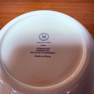 Op de afbeelding: Witte keramische kom met het Martha Stewart Collection-logo en de tekst "Dishwasher Safe Microwave Safe Will Get Hot in the Microwave Made in China."
