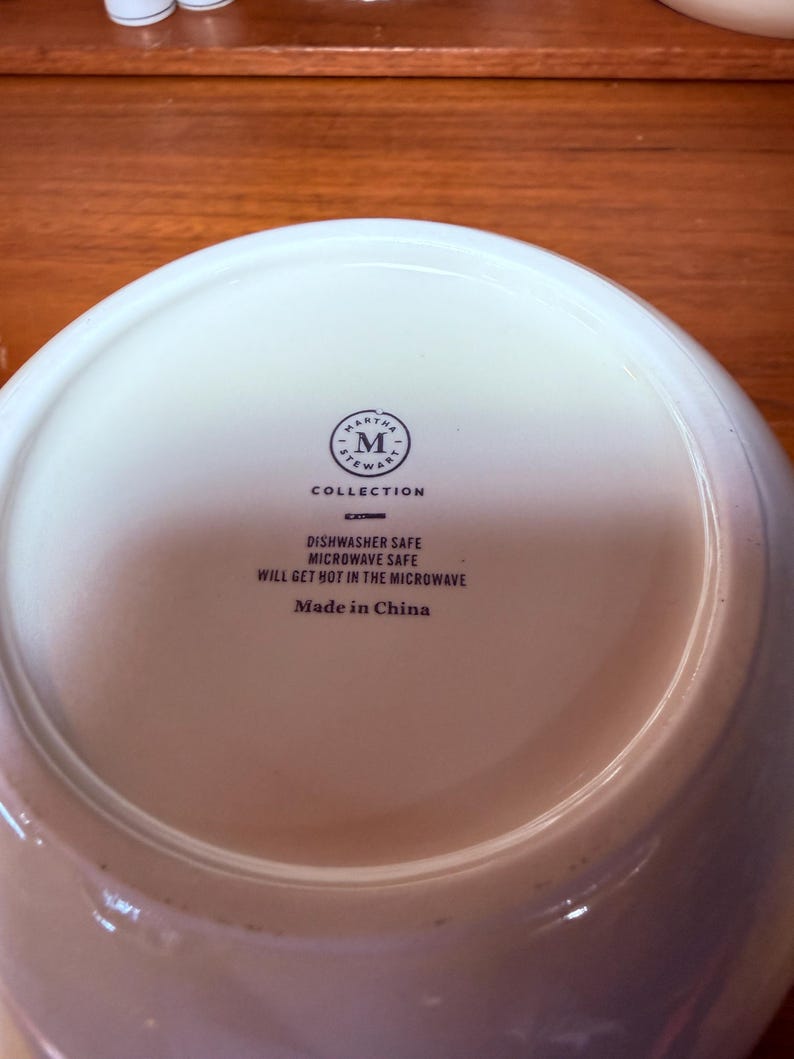 Op de afbeelding: Witte keramische kom met het Martha Stewart Collection-logo en de tekst "Dishwasher Safe Microwave Safe Will Get Hot in the Microwave Made in China."