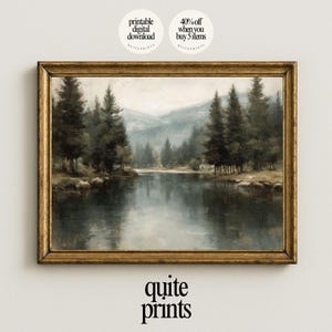 May include: A framed landscape print featuring a serene lake scene with tall evergreen trees and distant mountains. The artwork is in muted tones of green, gray, and brown, with a reflective lake surface. The frame is gold-colored. The print is labeled "quite prints".