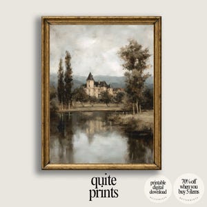 Puede incluir: Una impresión enmarcada de un paisaje con un castillo junto a un lago, rodeado de árboles. La obra de arte utiliza tonos apagados de gris, marrón y beige, en un marco dorado ornamentado. La impresión está etiquetada como "quite prints".