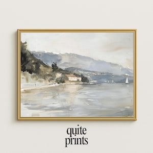 May include: A framed watercolor print of a coastal landscape. The artwork depicts a serene scene with mountains, a body of water, and sailboats. The color palette is soft, featuring muted blues, greens, and grays. The frame is gold, and the text "quite prints" is at the bottom.