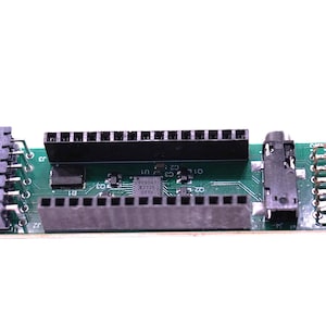May include: A green circuit board with various connectors, including a power connector, multiple pin headers, and a 3.5mm audio jack. The board has several integrated circuits and electronic components.