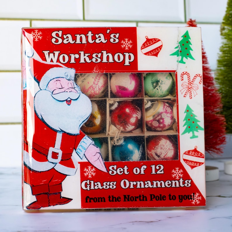 May include: A vintage box of 12 glass Christmas ornaments. The box is red and white with a Santa Claus illustration and the text "Santa's Workshop". The ornaments are in various colors and designs.