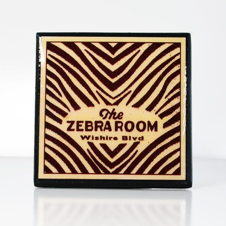 May include: A black and white zebra print square sign with the text "The Zebra Room, Wilshire Blvd" in red.