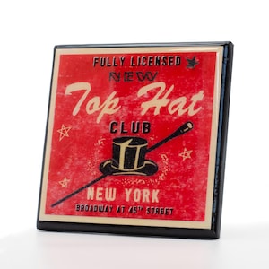 以下が含まれることがあります： 「Fully Licensed New York Top Hat Club Broadway at 45th Street」と黒文字で書かれた、赤と白のヴィンテージスタイルの看板。看板には、白いバンドが付いた黒いシルクハットと、黒い先端が付いた白い棒が描かれている。