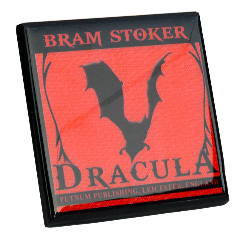 May include: Square black magnet featuring the title "DRACULA" and the author "BRAM STOKER" in white and gray text. A black bat silhouette is centered on a red background. The publisher's name and location are at the bottom.