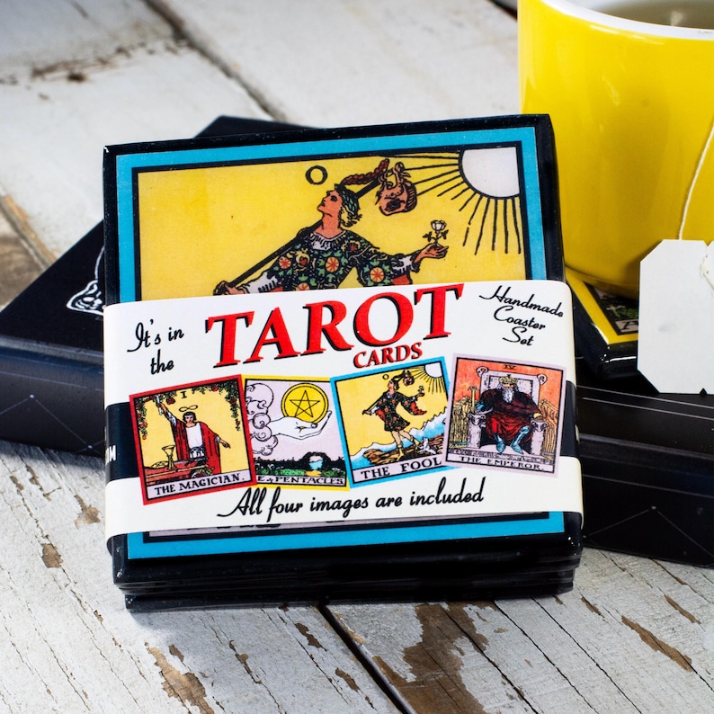 May include: A set of tarot card coasters. The coasters are black with a blue border and feature tarot card images. The set includes the Magician, Pentacles, the Fool, and the Emperor. The text "TAROT CARDS" is displayed on the front.