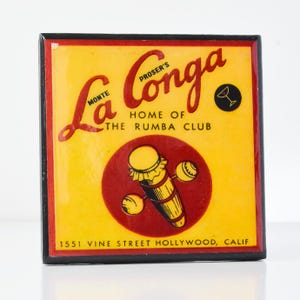 May include: A vintage-style sign for La Conga, Proser's Home of the Rumba Club, located at 1551 Vine Street Hollywood, Calif. The sign features a yellow background with red and black lettering. A red circle with a stylized illustration of a conga drum and maracas is in the center of the sign.