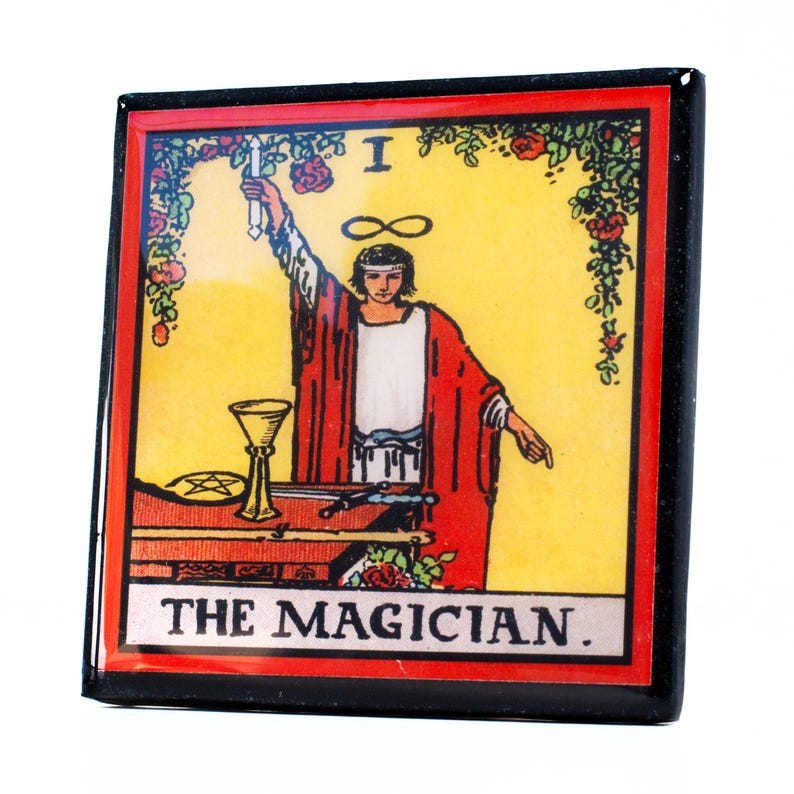 May include: Square magnet featuring a tarot card illustration of The Magician. The card has a yellow background with a figure in red robes, a chalice, and the infinity symbol. The text "THE MAGICIAN" is at the bottom, with a black border.