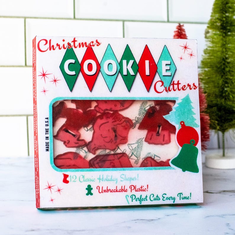 May include: A box of Christmas cookie cutters with red, green, and white accents. The box features the words "Christmas Cookie Cutters" and "12 Classic Holiday Shapes!" The cutters are red and visible through a window.