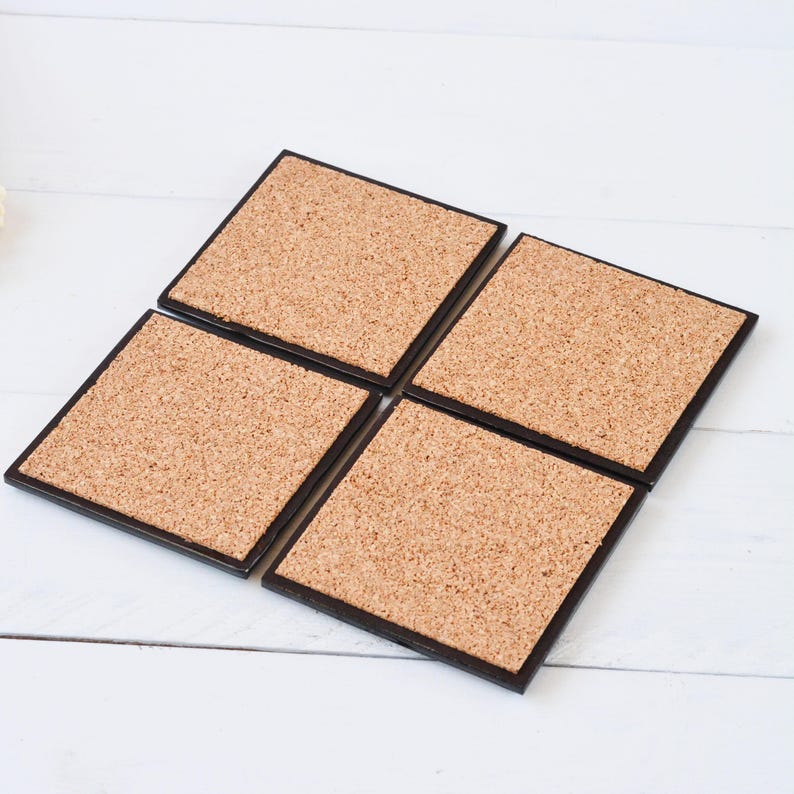 May include: Set of four cork coasters with black trim. The coasters are square and have a natural cork surface.