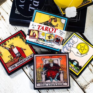 May include: A collection of tarot card coasters featuring vibrant illustrations and text. The coasters display images of The Magician, The Emperor, and other cards. The text "TAROT CARDS" is visible on a coaster, along with the phrase "All four images are included."
