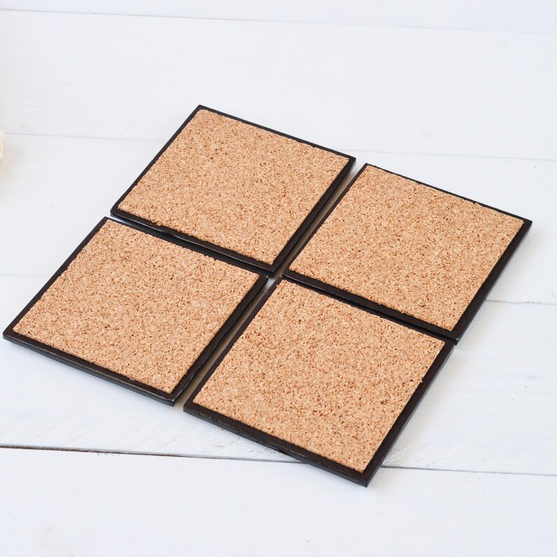 May include: Set of four cork coasters with black borders. The coasters are square shaped and have a natural cork surface.