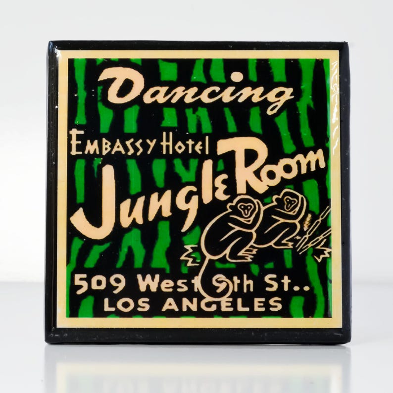 May include: A black and green sign with white lettering advertising the "Dancing Jungle Room" at the Embassy Hotel. The sign also includes the address "509 West 9th St., Los Angeles".
