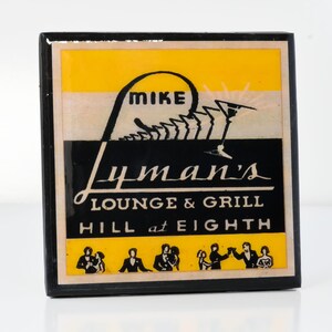 May include: A black and yellow square sign with the text "Lyman's Lounge & Grill Hill at Eighth" and a stylized image of a person with the word "Mike" above their head.