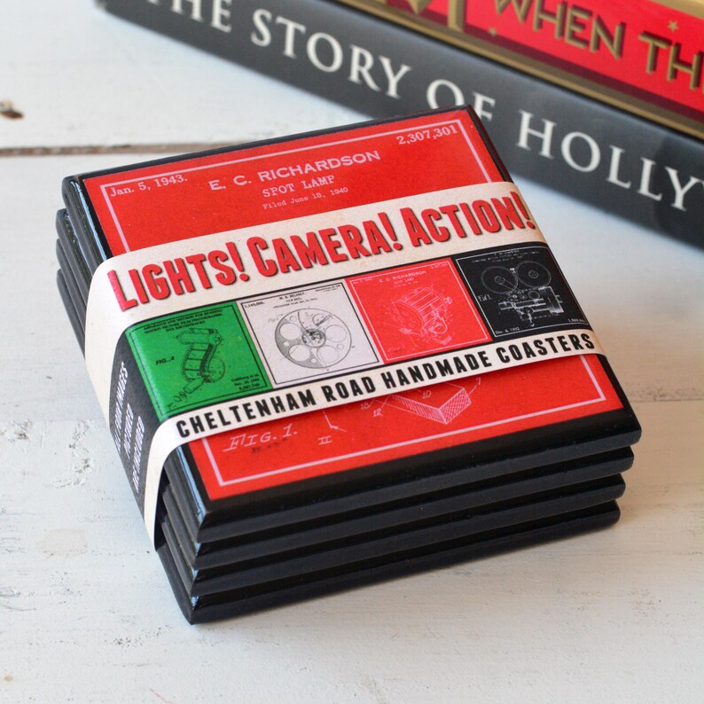 May include: Set of four black coasters with a red, white and green design. The coasters feature a vintage illustration of a film camera and the text "LIGHTS! CAMERA! ACTION!" and "CHELTENHAM ROAD HANDMADE COASTERS".