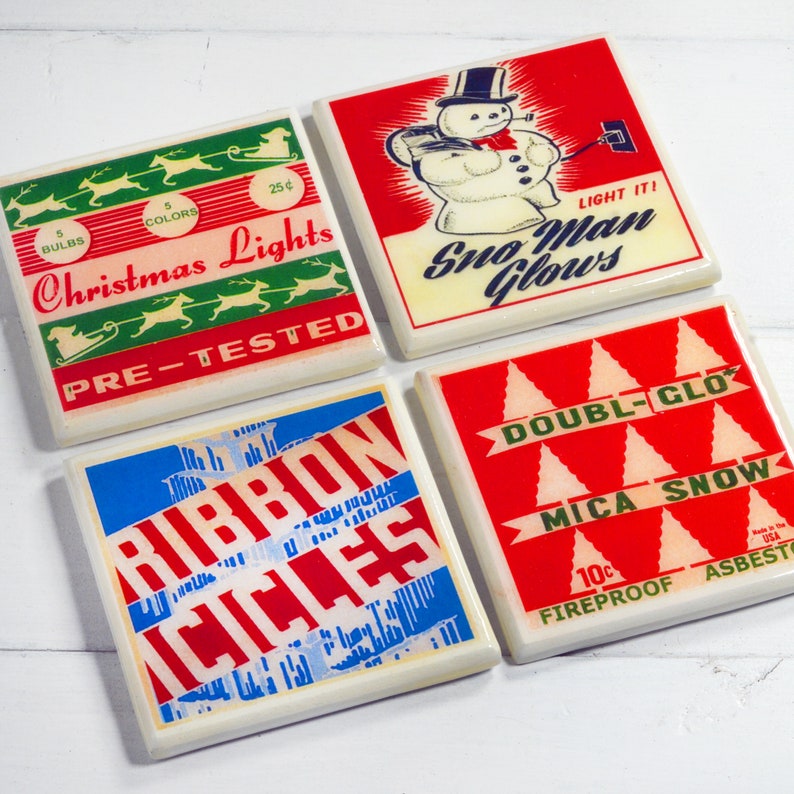 May include: Four vintage ceramic coasters with colorful designs. The first coaster features a green and red Christmas lights design with the text "Christmas Lights" and "Pre-Tested". The second coaster features a red and white snowman design with the text "Light It! Sno Man Glows". The third coaster features a blue and red design with the text "Ribbon Icicles". The fourth coaster features a red and white design with the text "Double-Glo Mica Snow" and "Fireproof Asbestos".