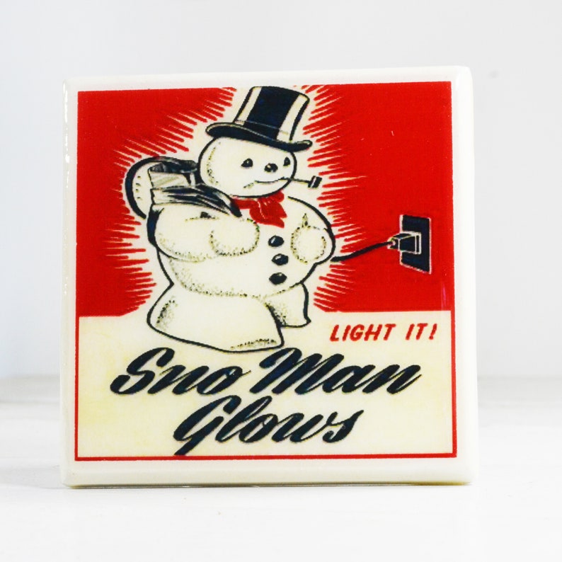 May include: A vintage-style illustration of a snowman with a black top hat and red scarf, holding a cord plugged into an electrical outlet. The text "Light It! Sno Man Glows" is printed below the snowman.