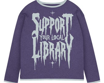 May include: A long-sleeved, purple sweatshirt with a light blue trim around the collar and cuffs. The front of the shirt features the text "SUPPORT YOUR LOCAL LIBRARY" in a stylized, light blue font, with star accents.