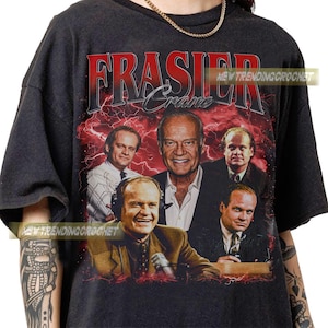 May include: Dark grey t-shirt with a graphic of the TV show "Frasier." The design features the show's title in red, along with images of the cast. The background has a red lightning effect.