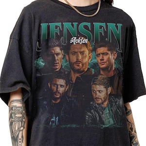 May include: Dark gray t-shirt featuring a collage of images of Jensen Ackles, with the name "JENSEN" in green block letters above the images. The word "Ackles" is in a smaller font. The shirt has a vintage, distressed look.
