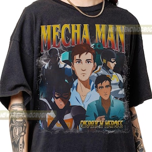 May include: Dark grey t-shirt with a graphic design. The design features the text "MECHA MAN" in yellow and red, and "DISPATCH HEROES" in gold. The graphic includes illustrations of several characters in superhero costumes.