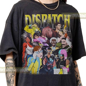 May include: Dark gray t-shirt featuring a colorful graphic of various cartoon characters with the word "DISPATCH" in yellow and white. The design includes a variety of figures in action poses.