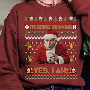 Może przedstawiać: Bordowy sweter świąteczny z świątecznym wzorem. Sweter zawiera tekst "I'M GOING DRINKING" i "YES, I AM!" wraz z obrazami czaszek, choinek, dzwonków i kufli piwa. Osoba w stroju Świętego Mikołaja pije ze szklanki.