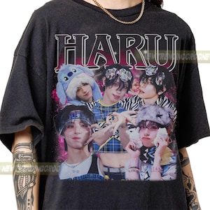 May include: Dark gray t-shirt featuring the word "HARU" in a retro font above a collage of five people. The people are wearing various hats and accessories, with a pink and purple background.