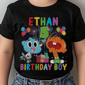 May include: Black t-shirt featuring a colorful graphic of cartoon characters, balloons, and fireworks. The text "ETHAN 5 BIRTHDAY BOY" is displayed in rainbow colors. The shirt is worn by a child.