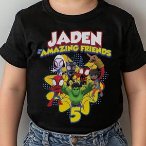 May include: Black t-shirt featuring the text "JADEN and his AMAZING FRIENDS" in white and yellow. The shirt has a graphic of several cartoon superheroes and the number 5 in yellow.