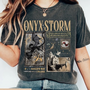May include: Pepper-colored t-shirt with the text "ONYX STORM" in gold lettering. The shirt features a graphic of a black dragon, a castle, and the words "BASGIATH WAR COLLEGE". The shirt also has the quote "A dragon without its rider is a tragedy. A rider without their dragon is dead."