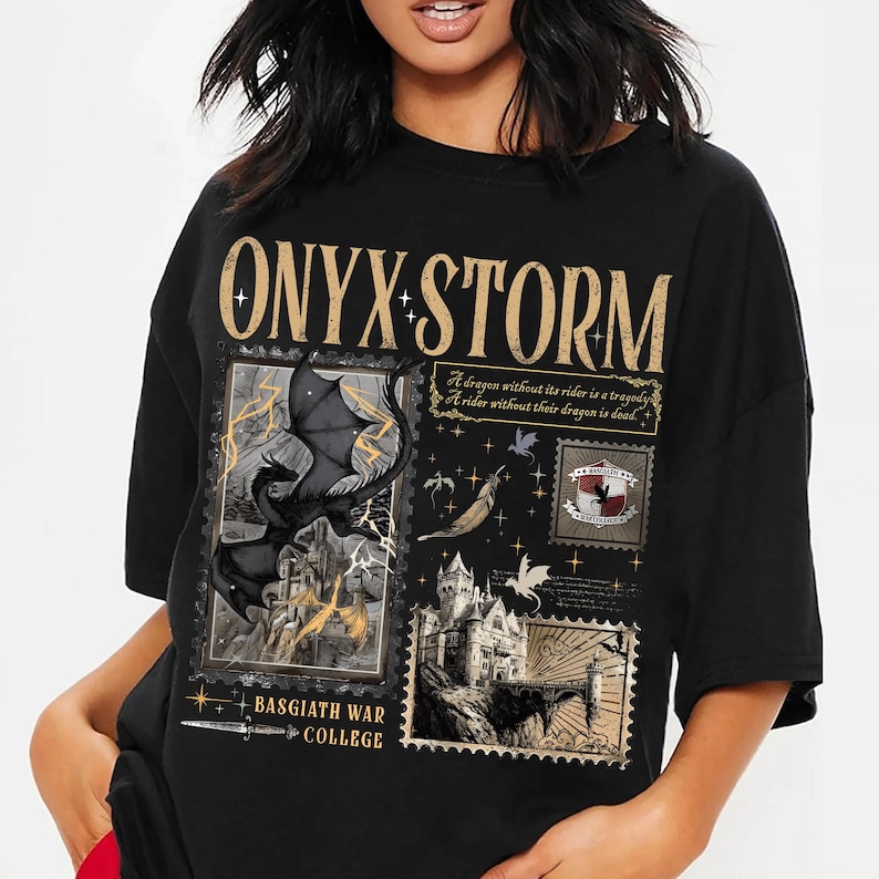 May include: Black t-shirt featuring a fantasy-themed design. The design includes the text "ONYX STORM" in gold lettering, along with illustrations of dragons, castles, and the text "BASGIATH WAR COLLEGE". The shirt has a crew neck and short sleeves.
