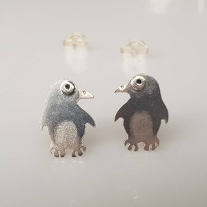 May include: A pair of silver penguin stud earrings. Each earring features a detailed penguin silhouette with a small black dot for an eye.