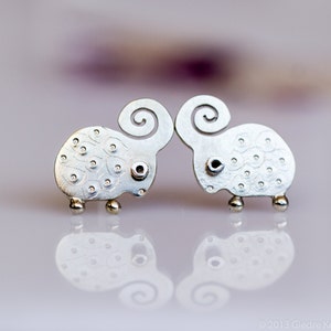 May include: A pair of silver earrings shaped like sheep with detailed textured surfaces. The sheep have curled horns and are facing each other.