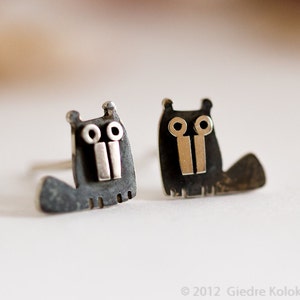 May include: A pair of silver earrings shaped like cartoon animals with black and silver details. The earrings are small and delicate.