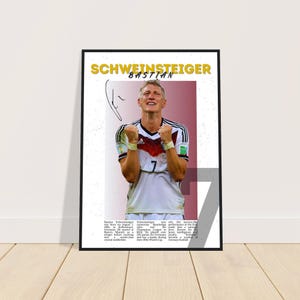 Op de afbeelding: Een ingelijste poster met een foto van Bastian Schweinsteiger in een wit en zwart voetbalshirt met nummer 7. De poster bevat de tekst "SCHWEINSTEIGER BASTIAN" in geel en wit.