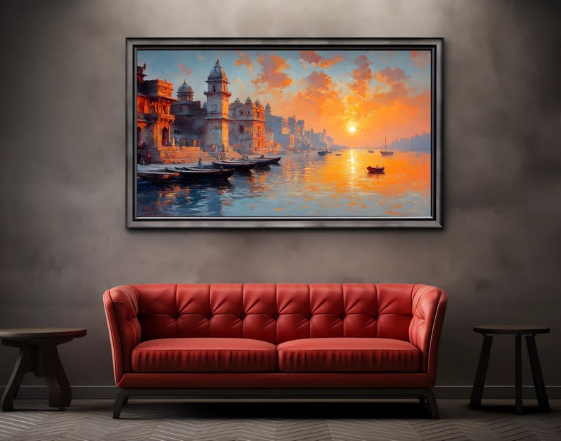 May include: A framed landscape painting depicts a vibrant sunset over a river with buildings and boats. The artwork is displayed above a red tufted sofa, with a dark gray wall and two small wooden side tables.
