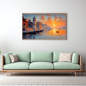 May include: A framed landscape painting depicts a vibrant sunset over a river with buildings and boats. The artwork is displayed above a light green sofa with beige pillows, complemented by a small side table and a potted plant, creating a serene living room scene.