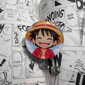 May include: A circular badge depicting a smiling cartoon character in a straw hat and red jacket. The badge is set against a black and white manga comic book background. The comic pages have speech bubbles and sound effects.