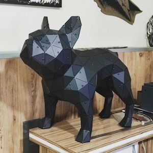 Può includere: Scultura geometrica in metallo nero di un bulldog francese. La statua del cane è costruita con forme triangolari e poligonali, con rivetti visibili. La scultura è su una superficie di legno.