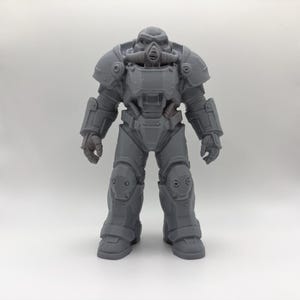 May include: A gray, unpainted resin figurine of a futuristic soldier in heavy, full-body power armor. The suit features a rounded helmet with a central breathing apparatus, broad shoulder pauldrons, articulated limb plating, and thick boots.