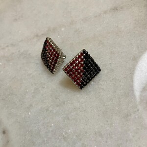 Peut inclure: Deux boucles d'oreilles carrées. Une boucle d'oreille est rouge et noire, l'autre est rouge. Les boucles d'oreilles sont faites de petites perles rondes. Les boucles d'oreilles sont sur une surface en marbre blanc.
