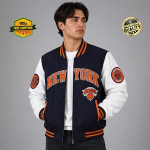 Pode incluir: Uma jaqueta varsity azul-marinho com mangas brancas e detalhes em laranja. A frente apresenta o texto NEW YORK em letras laranja, um logotipo do New York Knicks e emblemas circulares do Knicks em ambas as mangas. Fecho frontal com zíper.