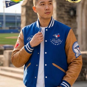 Puede incluir: Una chaqueta universitaria azul y marrón con rayas blancas en los puños y el cuello. La chaqueta presenta parches con texto y logotipos, incluyendo "OCD G&T DIVISION" y un logotipo de los Blue Jays. La chaqueta se lleva sobre una camisa blanca.