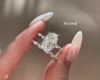 May include: A gold ring with a large oval-cut diamond and smaller accent stones. The ring is held up, showcasing its design. Text on the image reads "3ct oval" and "How our stylish clients stack their rings."
