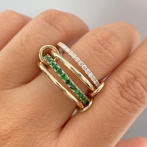Könnte beinhalten: Ein mehrreihiger Ring mit einem goldfarbenen Kettenglied-Design. Ein Ringband ist mit kleinen, runden, leuchtend grünen Edelsteinen besetzt, während ein anderes Band mit einer Reihe kleiner, klarer, funkelnder weißer Steine verziert ist.