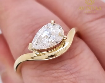 May include: A gold ring with a pear-cut diamond. The diamond is held in a bezel setting, and the band has a smooth, curved design. The ring is a piece of jewellery.