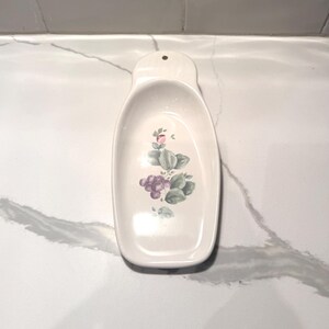以下が含まれることがあります： 紫色のブドウ、緑の葉、ピンクの花をあしらったフローラルデザインの白いセラミック製スプーンレスト。 レストは、吊り下げ用のハンドルと穴が付いた長い楕円形をしています。 装飾的なキッチンアクセサリー。